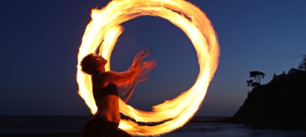 Foto föreställande kvinna som jonglerar med eld på en strand.